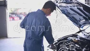 年轻的亚洲汽车机械师在汽车修理<strong>车间</strong>的汽车引擎盖检查发动机。 维修人员检查客户<strong>安全</strong>